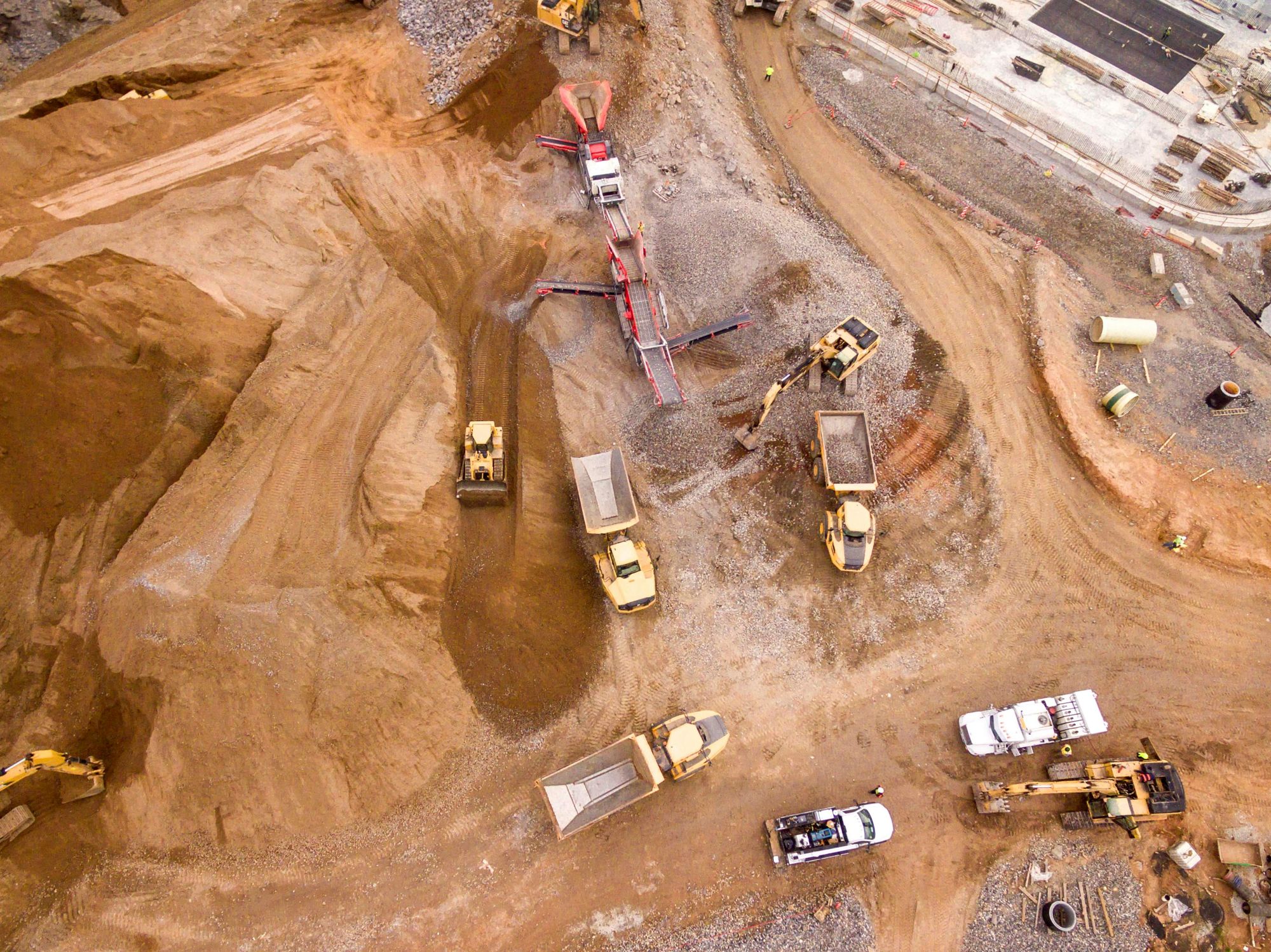 Vista aérea de una obra con camiones articulados, excavadoras y una planta de cribado en operación