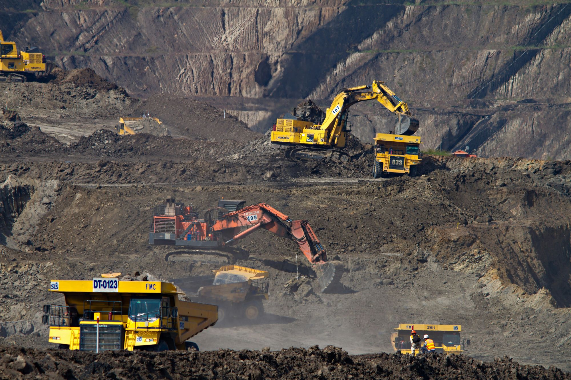 Excavadoras hidráulicas cargando camiones mineros en distintos bancos de una mina a cielo abierto